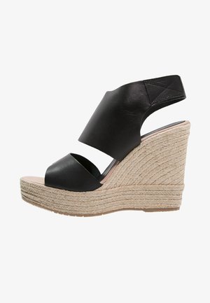 Sandalias de cuña negras de cuero con una banda ancha sobre el pie, plataforma con textura de cuerda y una altura de aproximadamente 10 cm.