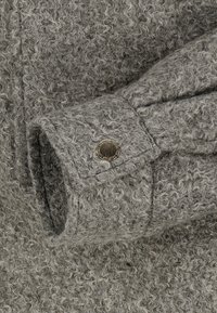 Gray woolen fabric close-up with a textured, curly pattern. Features a metal button on the sleeve cuff, enhancing detail and design.