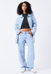 Light blue denim jacket and matching wide-leg jeans, paired with a black cropped top and white sneakers. Fabric is soft with a relaxed fit.