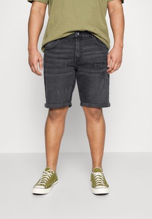 Schwarze Jeansshorts mit einem distressed Design, umgeschlagenen Säumen und Fünf-Taschen-Style, kombiniert mit olivgrünen Leinenschuhen.