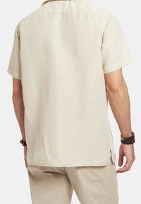 Košile s krátkým rukávem a límečkem v světlé béžové lněné tkanině. Volný střih se rovnými lemy a postranními rozparky, který zvýrazňuje hladkou textura.