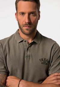 Grijze polo met een kraag, voorzien van een geborduurd "Texas Outlaw" logo in donkere draad, knoopsluiting en een gestructureerde stof.