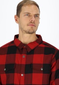 Rood en zwart geruite blouse met kraag, twee borstzakken en zilveren metalen knopen. Gemaakt van een gestructureerde stof.