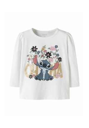 Chemise blanche à manches longues avec le personnage de dessin animé Stitch, des fleurs colorées et le mot « ohana » en grandes lettres dorées sur le devant.