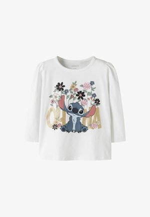 Chemise blanche à manches longues avec le personnage de dessin animé Stitch, des fleurs colorées et le mot « ohana » en grandes lettres dorées sur le devant.