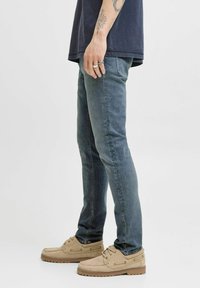 Mäns slim-fit jeans i mörkblå denim. Har en medelvatten, subtil blekning och femfickdesign. Kombineras med beige mockaskor.