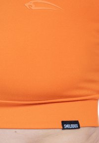 Oranje sportieve cropped top gemaakt van gladde stof. Heeft een subtiel logo en een zwart label aan de zoom. Geen zichtbare patronen of metalen details.