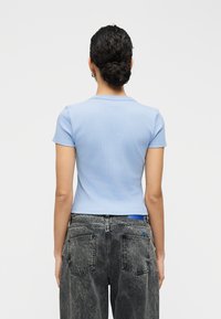 Ανοιχτό μπλε ριμπ κοντομάνικο τοπ με εφαρμοστή σχεδίαση, συνδυασμένο με ψηλόμεσα ξεβαμμένα γκρι τζιν, με μπλε ταμπέλα και πίσω τσέπες.