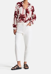 Camicia a maniche lunghe con un motivo di foglie di palma rosse su uno sfondo crema, abbinata a pantaloni dritti bianchi e sandali neri scivolati con fibbie.