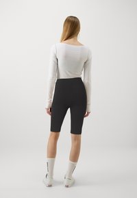 Långärmad, ljusgrå topp i kombination med svarta cykelshorts med hög midja. Modellen bär vita strumpor och sneakers. Enkel design, mjuk textur.