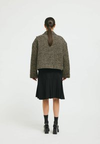 Jachetă scurtă, texturată, cu un model houndstooth, având mâneci ample, purtată peste o fustă neagră plisată și asortată cu pantofi cu toc bloc.