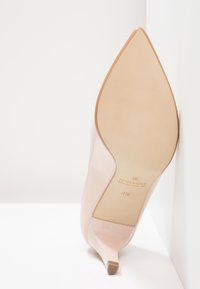 Escarpins en cuir verni rose pâle avec un bout pointu et un talon fin ; présentant une semelle beige avec le logo de la marque et les détails de taille.