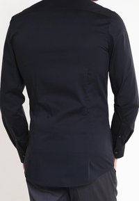 Camicia blu navy a maniche lunghe realizzata in tessuto liscio; presenta un colletto strutturato, polsini con bottoni e un leggero strascico all'orlo.