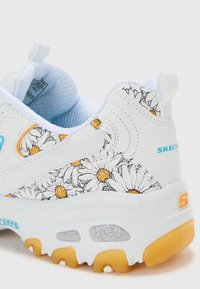 Chaussure de sport blanche avec un motif floral en noir et jaune, dotée d'un intérieur rembourré, d'une semelle texturée et d'accents orange et bleu.
