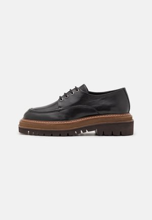 Zapato negro de cuero con cordones, suela gruesa marrón y oscura con relieve, acabado liso y punta redondeada, mostrado de perfil sobre fondo blanco.
