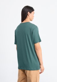 Męska koszulka krótki rękaw, zielona bawełna, luźny krój, okrągły dekolt, z gładką fakturą i wykończonymi rękawami. Pokazany widok z tyłu.