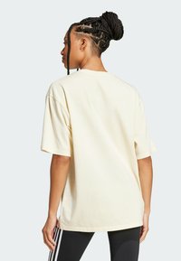 Světle žluté oversized bavlněné tričko s krátkými rukávy, kulatým výstřihem a volným střihem, zobrazené zezadu s černými legínami.