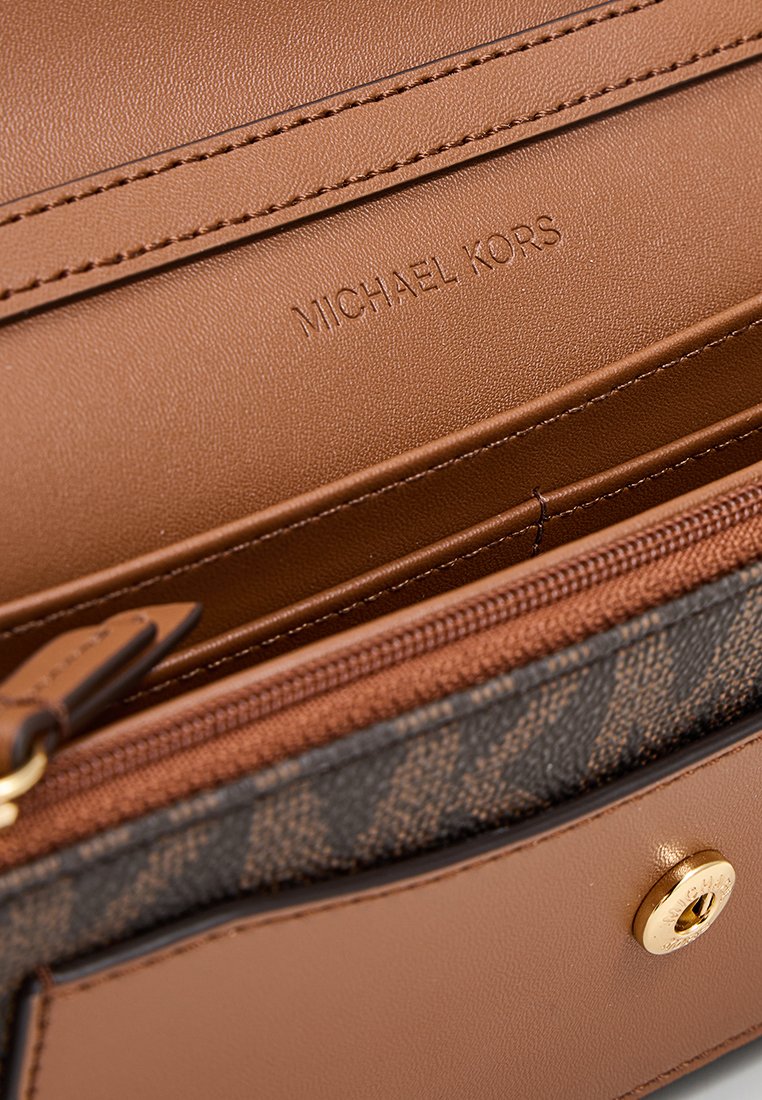 Braune Lederbörse mit tanfarbenen Akzenten, besitzt ein geprägtes "MICHAEL KORS"-Logo, ein Reißverschlussfach und ein charakteristisches Muster an der Seite.