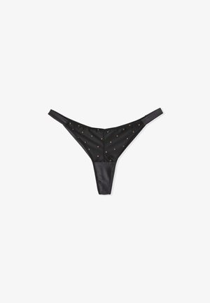 Black thong made of satin, featuring a smooth texture and small, metallic dot embellishments across the front. Adjustable straps.