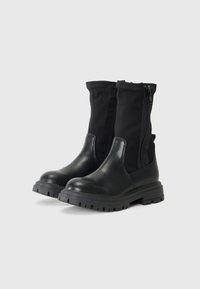 Bottines noires avec une semelle épaisse et une fermeture éclair sur le côté, alliant cuir et tissu pour un style moderne et polyvalent.