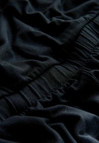 Close-up of black fabric with gathered elastic stitching creating textured, ruched folds and soft shadows.