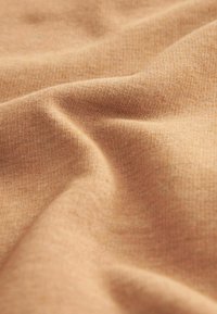 Kangas yang ditenun polos dalam warna coklat muda hangat, dengan tekstur lembut, sedikit meregang, dan variasi nada yang halus.