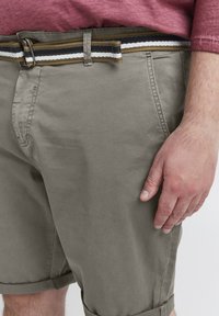 Shorts gris clair en coton avec une texture lisse. Comprend une ceinture tissée à rayures marron, marine et blanche et des ourlets roulés.