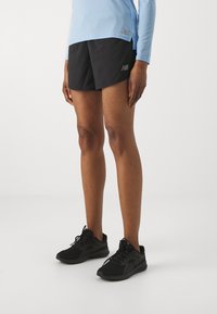 Black athletic shorts feature a lightweight, textured fabric. Paired with black running shoes, ideal for active wear. Light blue long-sleeve top.