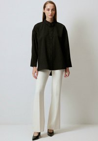 Black and white striped button-up shirt with long sleeves, paired with white flared pants and black pointed-toe heels. Smooth fabric texture.