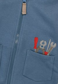 Blaues Zip-Up-Sweatshirt mit kleiner Fronttasche, die bestickte Werkzeuge zeigt: einen roten Schraubendreher, einen grauen Schraubenschlüssel und einen silbernen Pickel. Aus Baumwollmaterial.