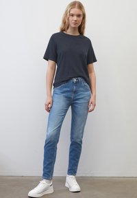T-shirt navy à manches courtes, jeans clairs délavés et baskets blanches. La tenue présente une coupe décontractée et un design minimaliste.