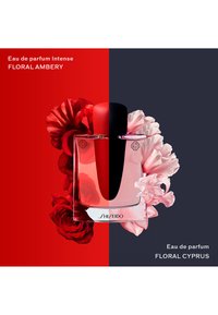 Botella de perfume centrada entre fondos rojo y oscuro, rodeada de rosas rojas a la izquierda y flores de color rosa pálido a la derecha.