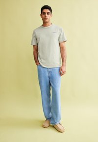 Lichtgroene katoenen T-shirt met korte mouwen, gecombineerd met blauwe denim jeans en beige instap schoenen. Eenvoudig ontwerp met minimale details.