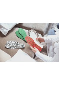 Sottopiedi in schiuma di vari colori: verde, bianco, a scacchi rossi, a strisce zebrate e a stampa leopardata, disposti su un divano beige con cuscini.