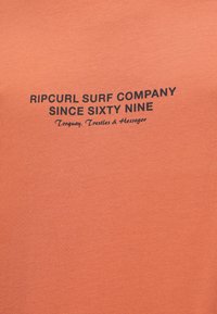 Tricou cu mânecă scurtă, de culoare coral, fabricat din bumbac, având un logo tipărit negru cu textul: "RIP CURL SURF COMPANY DIN ȘAIZECI ȘI NUE."