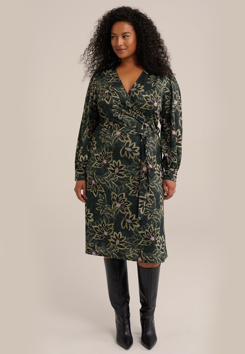 Rochie tip wrap din material verde închis, cu modele florale în tonuri de aur și violet. Mâneci lungi, talie accentuată și tiv până la genunchi. Botine negre până la genunchi.
