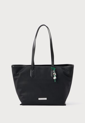 Melna roku soma ar dubultajiem plecu siksnām un nelielu zaļas un baltas krāsas tēlu piekariņu, kas karājas pie vienas siksnas.