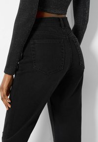 Högmidjade svarta jeans i denim med rak passform, utrustade med två bakfickor och en strukturerad yta.