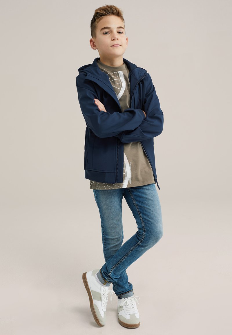 Mornarska zip-up jopica s kapuco, siva grafična majica, modre skinny kavbojke, bele superge s sivimi poudarki. Obleka za prosti čas za mlade.