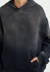 Hoodie noir avec une texture décolorée et usée. Dispose d'une poche avant et d'une capuche avec cordon de serrage. Tissu doux avec une coupe décontractée.