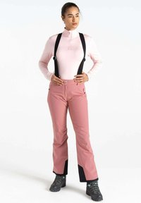 Helles rosa Langarmshirt mit einem Viertelreißverschluss, kombiniert mit pinken Skihosen mit schwarzen Akzenten und verstellbaren schwarzen Hosenträgern.