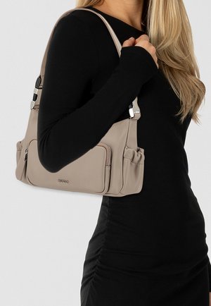 Beige leren schoudertas met zilveren hardware, voorzien van twee zijvakken en een ritssluiting, gedragen op de schouder.