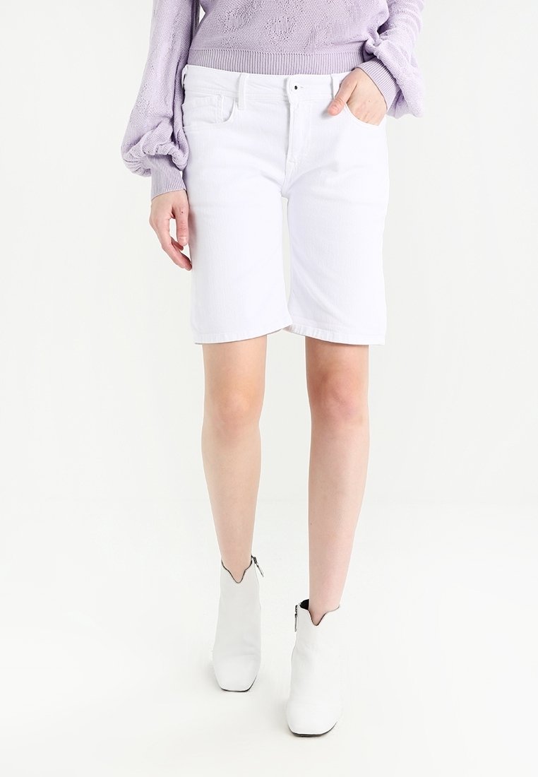 Bílé džínové šortky s přímým střihem, s předními kapsami a zipem, doplněné světle fialovým svetrem a bílými kotníkovými botami.