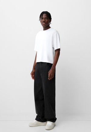 T-shirt en coton blanc, coupe décontractée, manches courtes. Jean en denim noir, silhouette large, poches avant. Baskets de couleur claire.