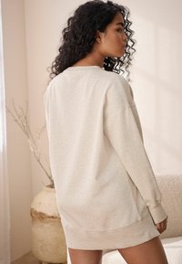 Jasno beżowa, oversize'owa sukienka typu sweatshirt wykonana z miękkiego materiału, z okrągłym dekoltem, długimi rękawami oraz ściągaczami u rękawów i na dole.