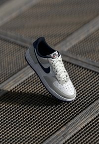 Nike Air Force 1 tenisice s gornjim dijelom od sive kože i mrežice, mornarsko plavim naglascima, bijelim vezicama, perforiranim prednjim dijelom i teksturiranim gumiranim potplatom.
