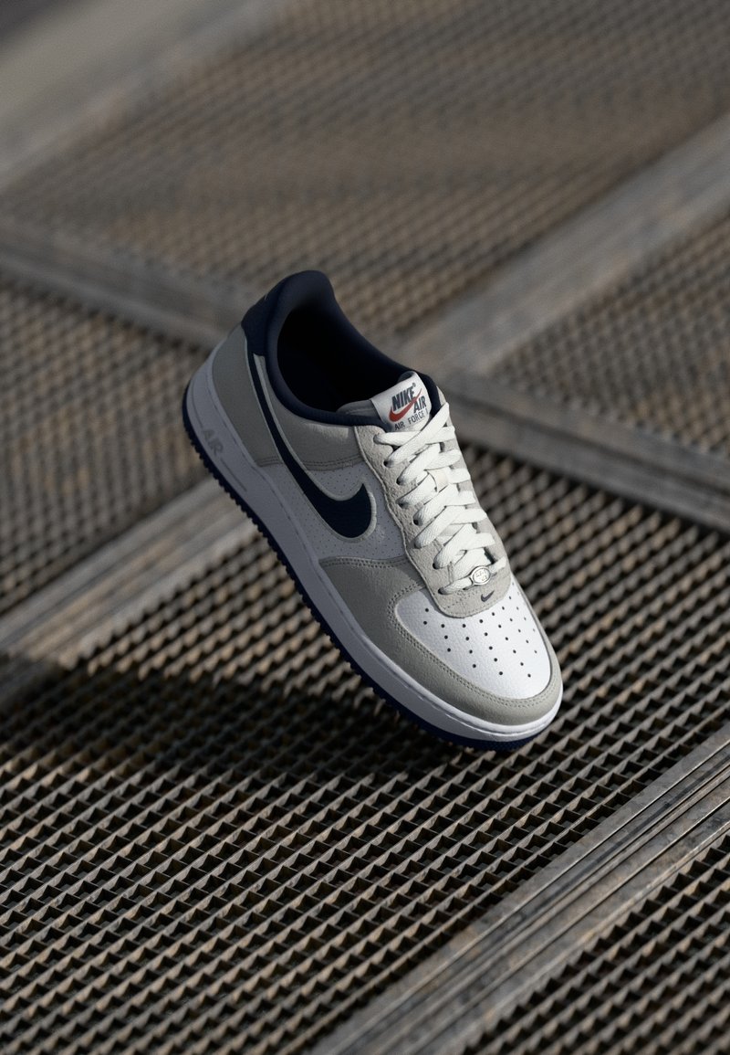 Nike Air Force 1 sneaker, millel hallist nahast ja võrkpinna ülemine osa, tumesinised aktsendid, valged paelad, perforatsioonidega varbakast ja tekstureeritud kummist välistald.
