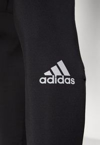 Black athletic leggings featuring a smooth texture, fitted design, and a prominent white Adidas logo on the lower leg.