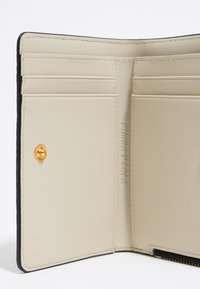 Interno di portafoglio in pelle beige con più slot per carte. Caratterizzato da un dettaglio con bottone a scatto dorato e logo del marchio stampato. Texture liscia.