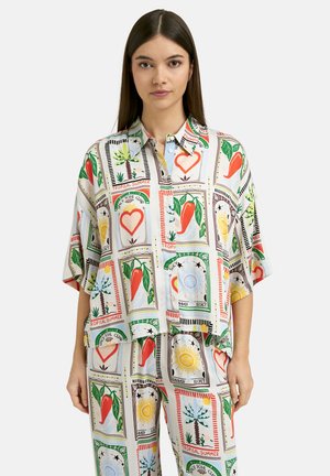 Young woman wearing a two-piece set with loose shirt and pants featuring colorful tropical prints of chili peppers, hearts, suns, and palm trees.
